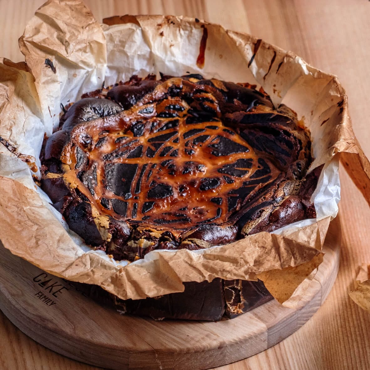 Шоколадно-апельсиновий Баскський чизкейк Cheesecake Family з темною припаленою скоринкою та рудуватими візерунками на пергаменті