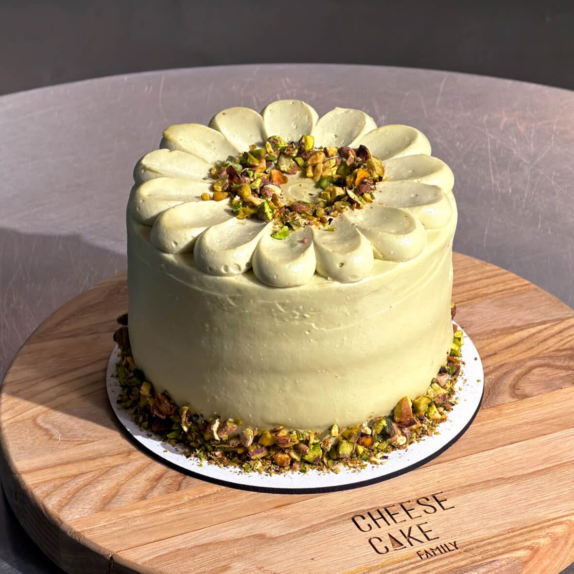 Бенто торт Фісташка-Малина від Cheesecake Family на дерев'яній підставці з ніжно-зеленим фісташковим кремом і декором із фісташкових горіхів.